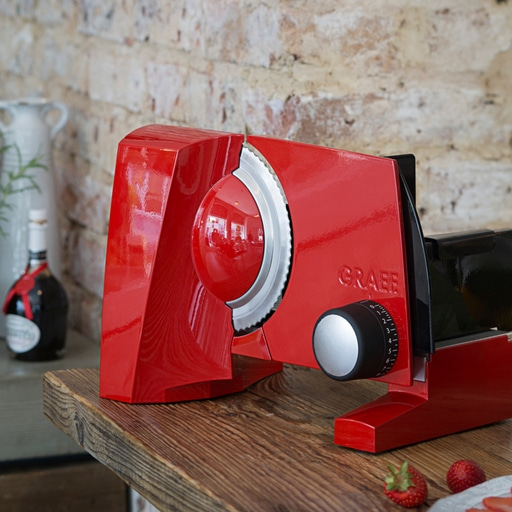 Red slicer on a wooden table with strawberries and a bottle in the background.