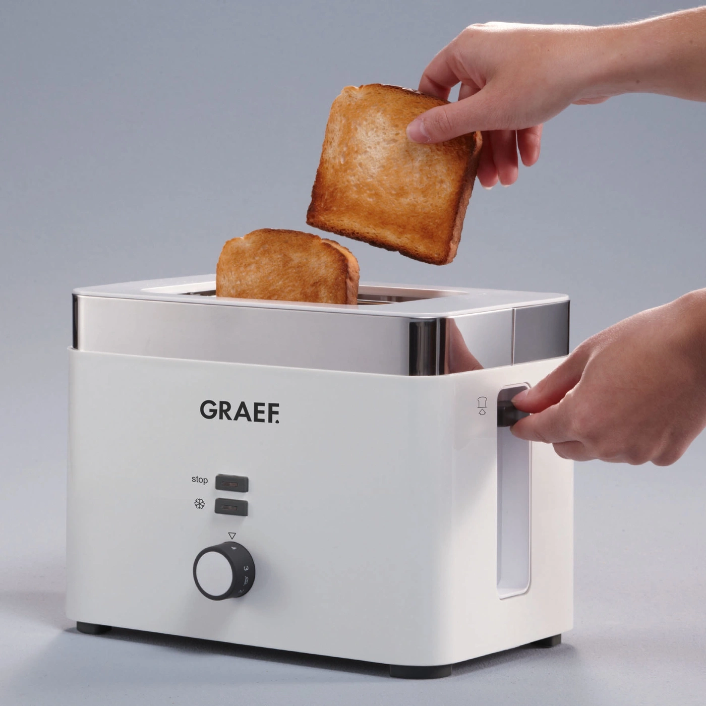 Weißer Toaster mit Toastbrot, das aus dem Toaster herausgeholt wird, und einer Hand, die den Knopf dreht.