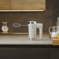 Ein weißer Handmixer steht auf einer Küchenarbeitsplatte neben einem Krug Milch.