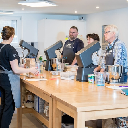 Bäckerei-Workshop: Menschen arbeiten an Holztischen mit Küchengeräten.
