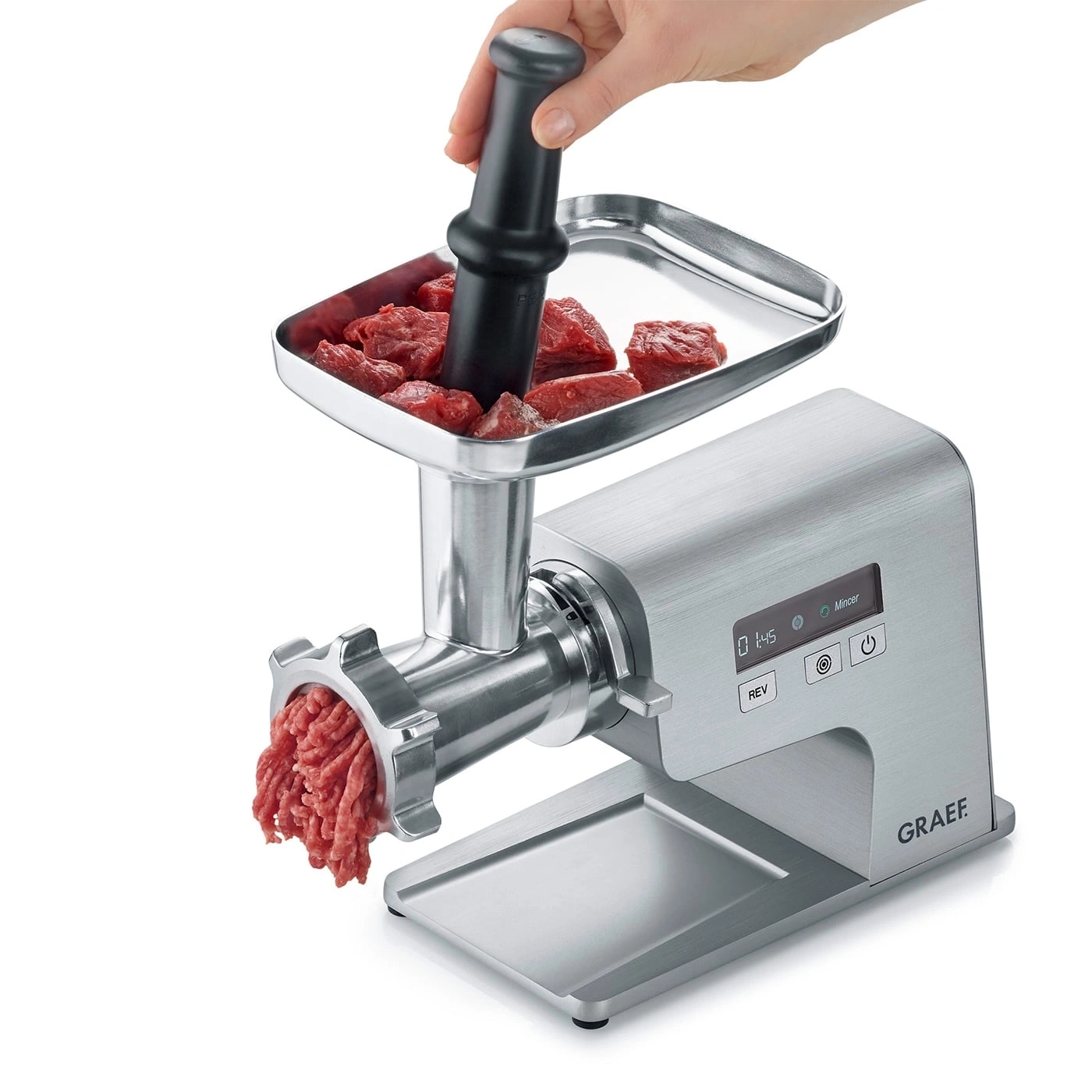 Fleischwolf mit Fleisch und Hand, die einen Stopfer benutzt, um Fleisch zu verarbeiten.