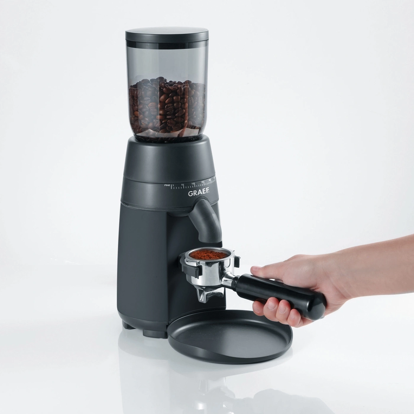Kaffeemühle mit Kaffeebohnen und Kaffeepulver, Hand hält Siebträger