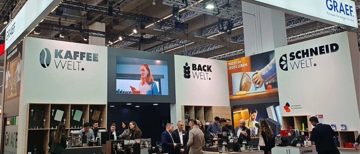 Kaffee- und Backwelt-Stand mit Menschen und Logos.