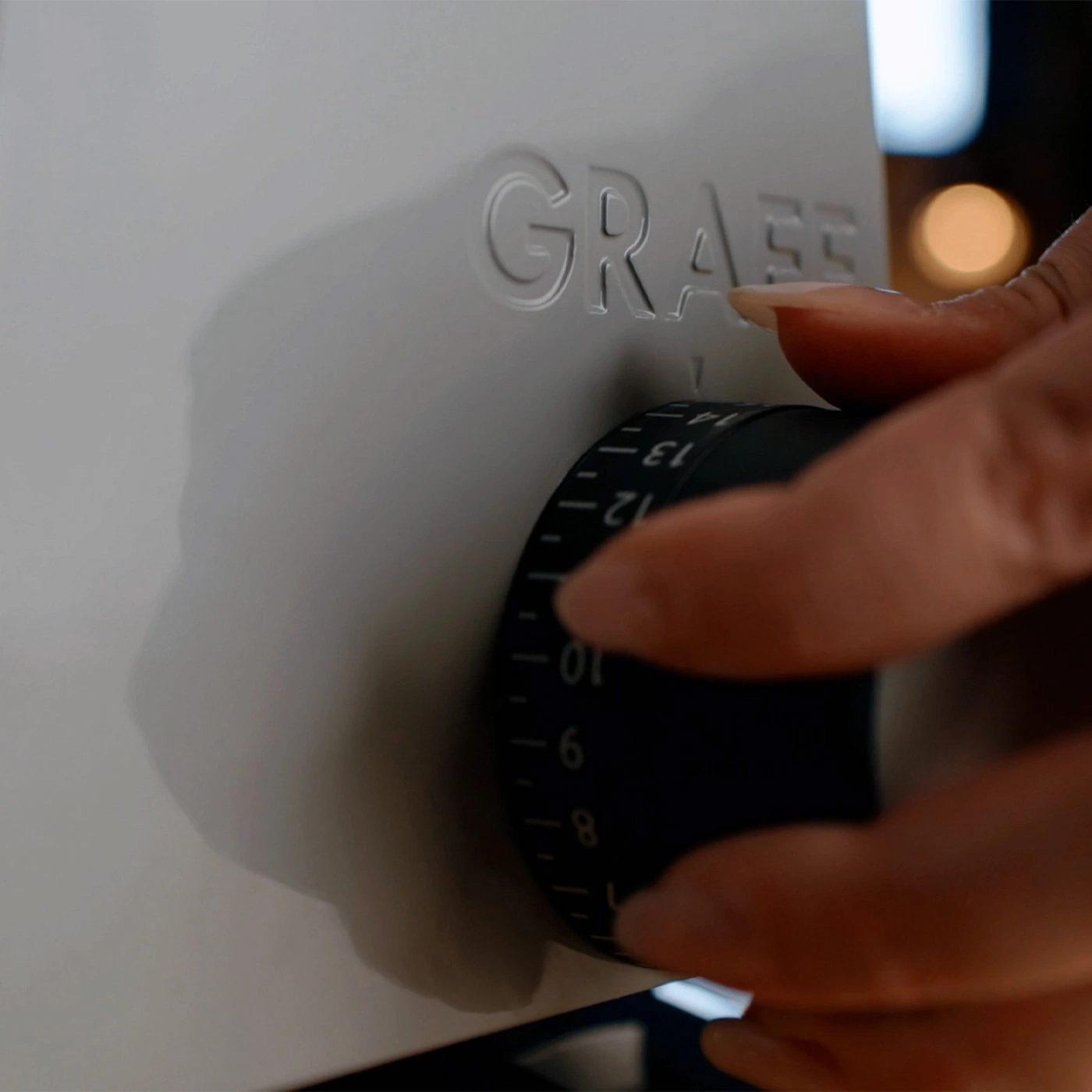 Eine Hand dreht einen Regler mit Zahlen auf einem weißen Gerät mit der Aufschrift GRAEF.
