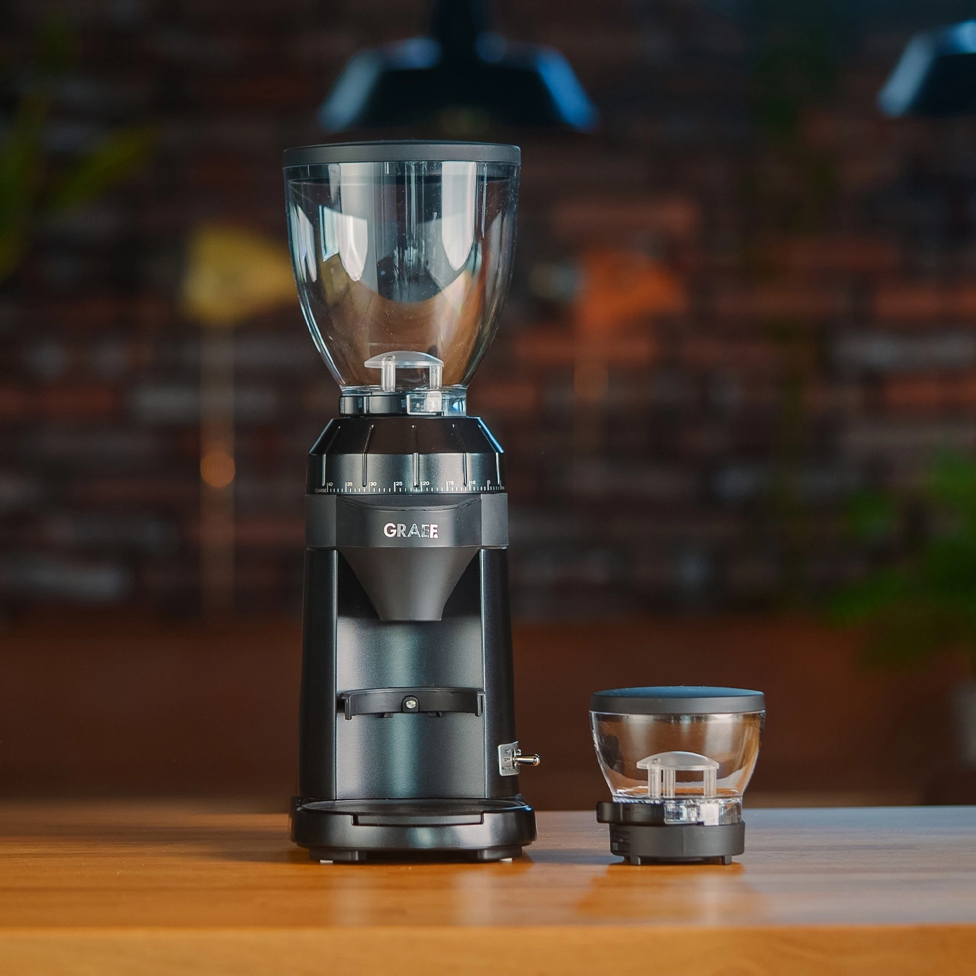 Zwei schwarze Kaffeemühlen, eine große und eine kleine, auf einem Holztisch.