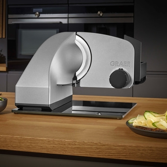 Graef Allesschneider auf Holztisch mit Essen und Küchengeräten im Hintergrund