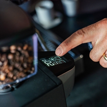 Hand drückt Knopf an Kaffeeröster, zeigt Temperatur und Zeit an.