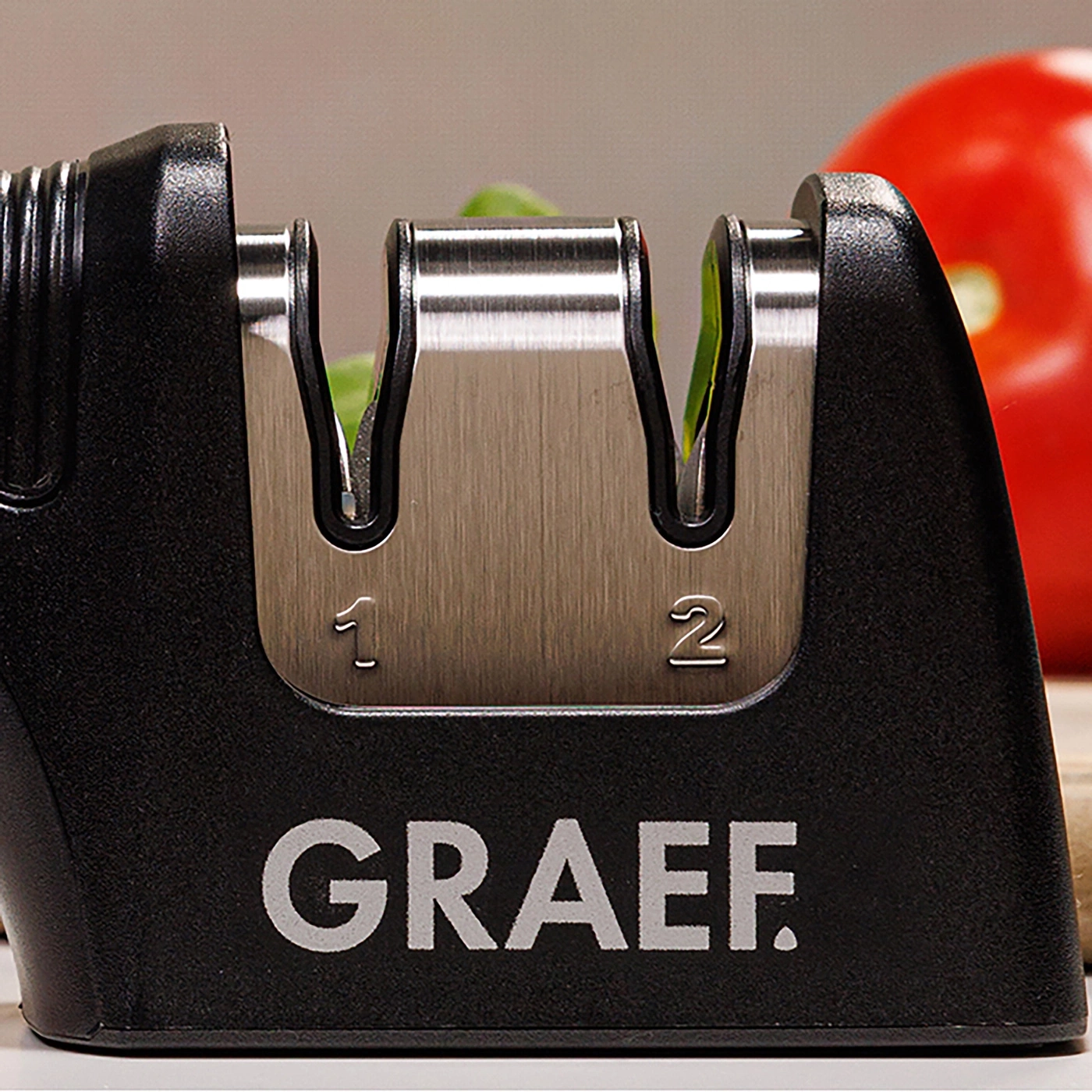 Ein Graef Messerschärfer mit den Zahlen 1 und 2, daneben ein roter Tomate.