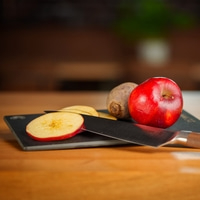 Apfel, Messer und Rote Bete auf einem Schneidebrett auf einem Holztisch