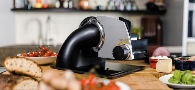 Trancheuse Graef avec tomates, pain, fromage et saucisse sur une table en bois