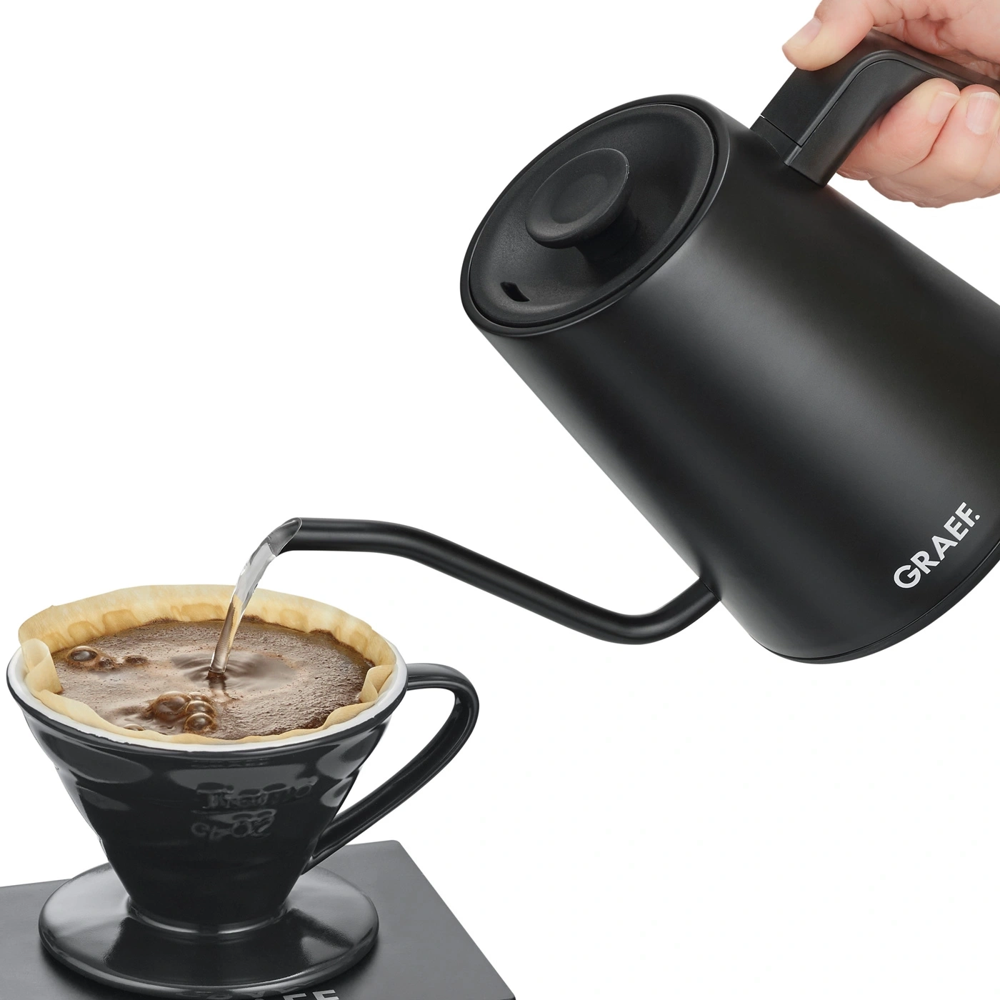 Schwarzer Wasserkocher gießt Kaffee in eine Tasse mit Filterpapier.