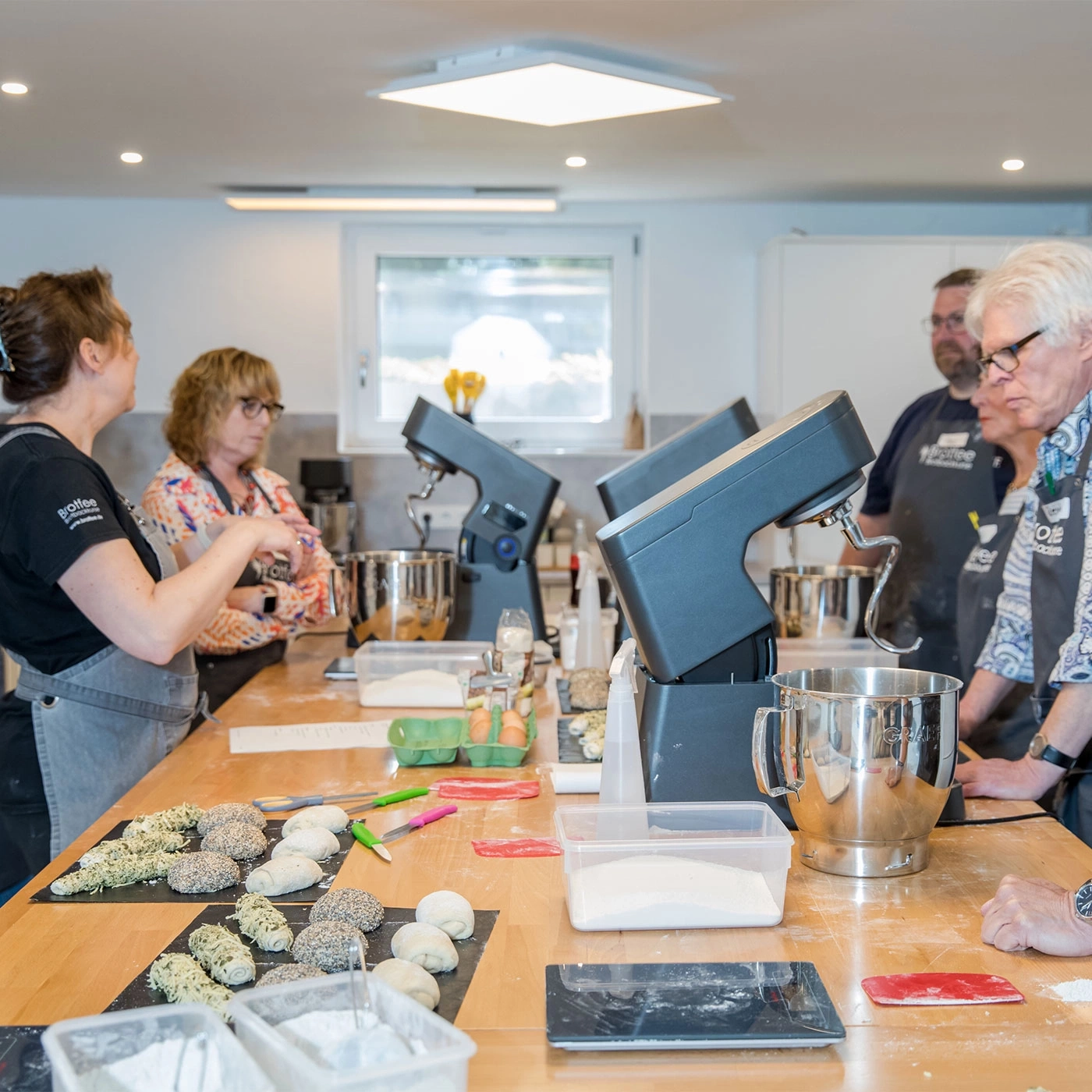 Bäckerei-Workshop: Menschen arbeiten an einem Tisch mit Zutaten und Geräten.