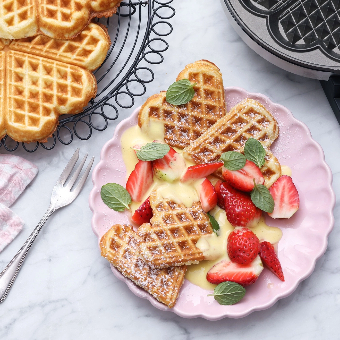 Herz-Waffeln mit Erdbeeren und Vanillesauce auf einem Teller.