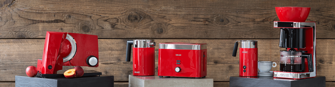 Red kitchen appliances on wooden background: coffee maker, toaster, milk frother, etc.