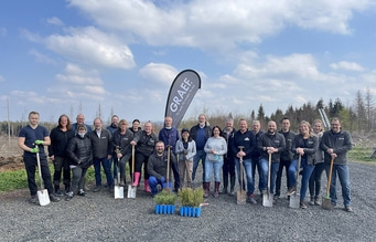 Gruppe von Menschen mit Spaten vor Bäumen und Banner mit Logo
