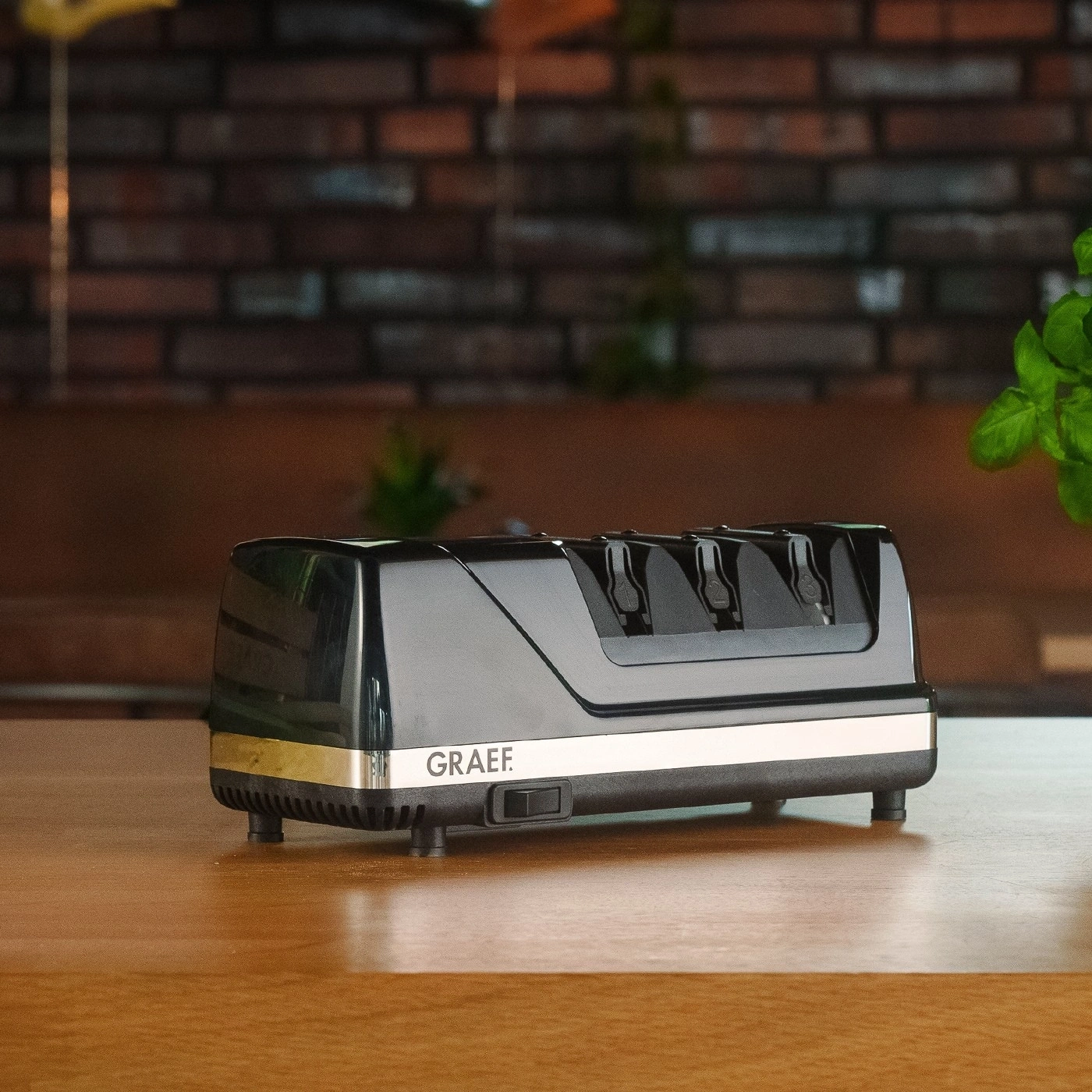 Schwarzer elektrischer Messerschärfer auf einem Holztisch mit GRAEF-Logo.