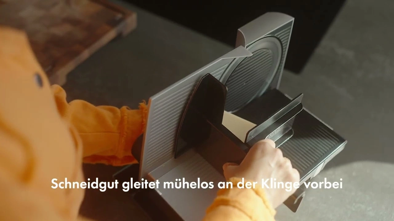 Nahaufnahme einer Person, die eine elektrische Aufschnittmaschine bedient, mit Text.