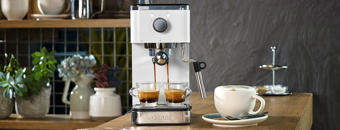 Macchina per espresso con due tazze, cappuccino e decorazioni su un tavolo di legno
