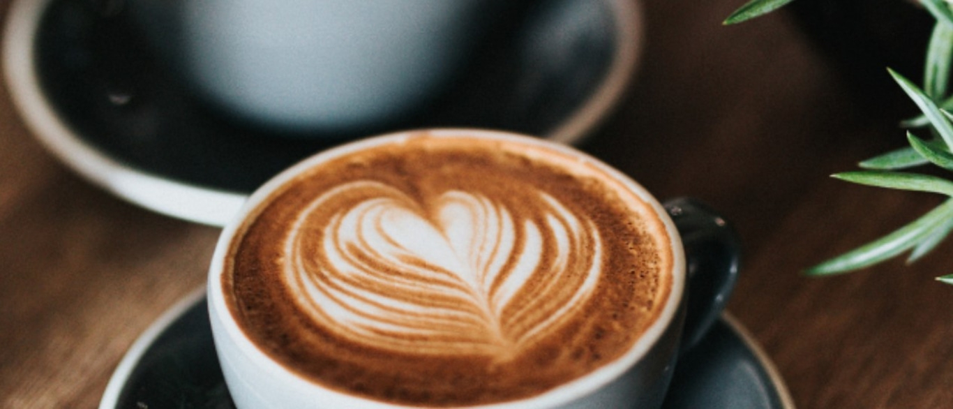 Kaffee mit Herzmuster, Nahaufnahme, auf einem Unterteller, Holzuntergrund