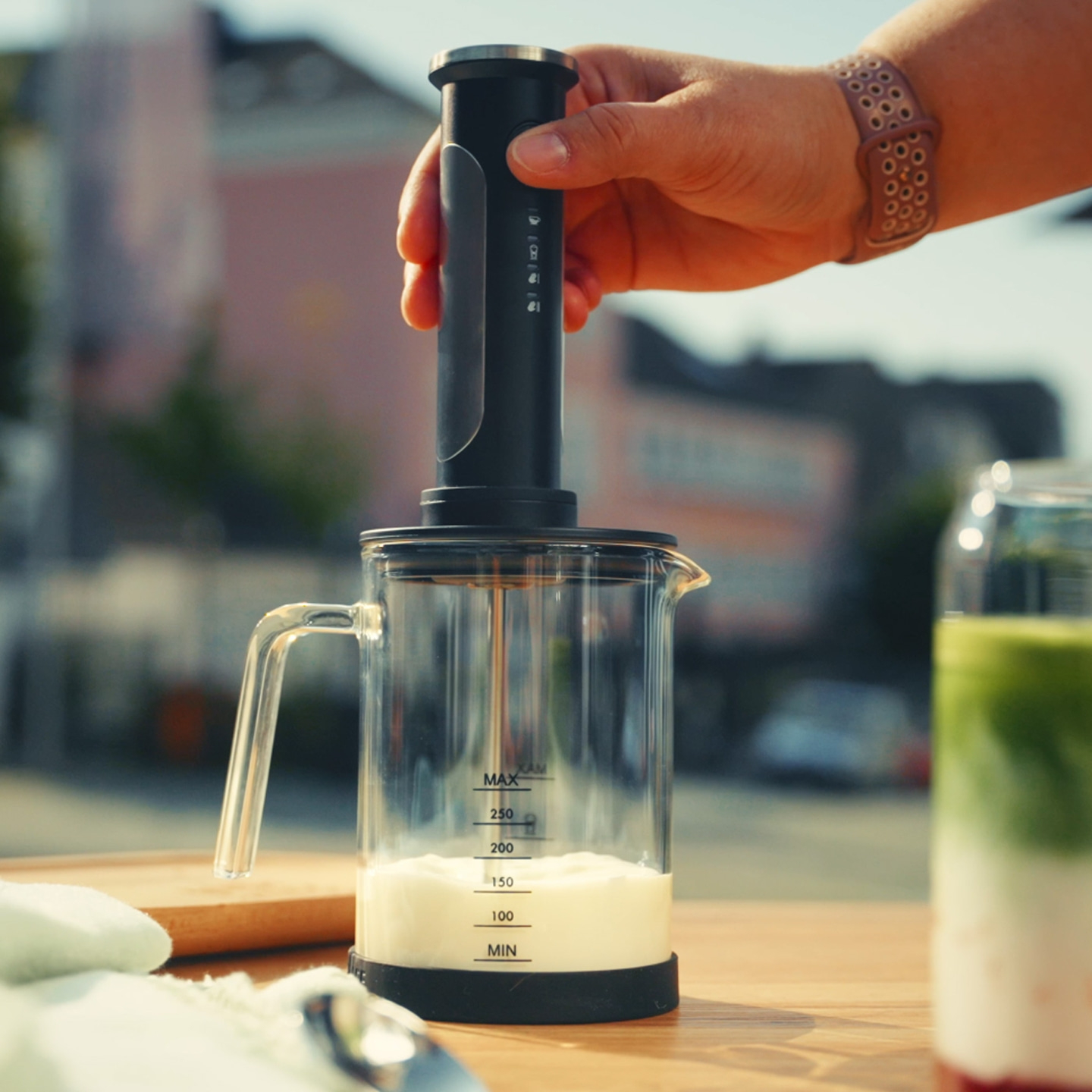 Eine Hand hält einen Milchaufschäumer über einem Glas mit Milch.