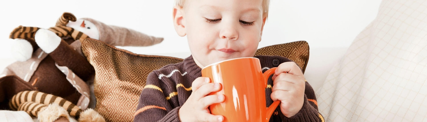 Bambino che beve da una grande tazza arancione, accogliente su un divano.