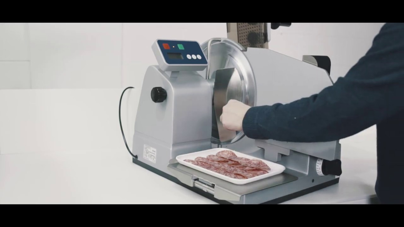Meat slicer slicing salami. Person operating machine. Slices on tray. Silver machine.
