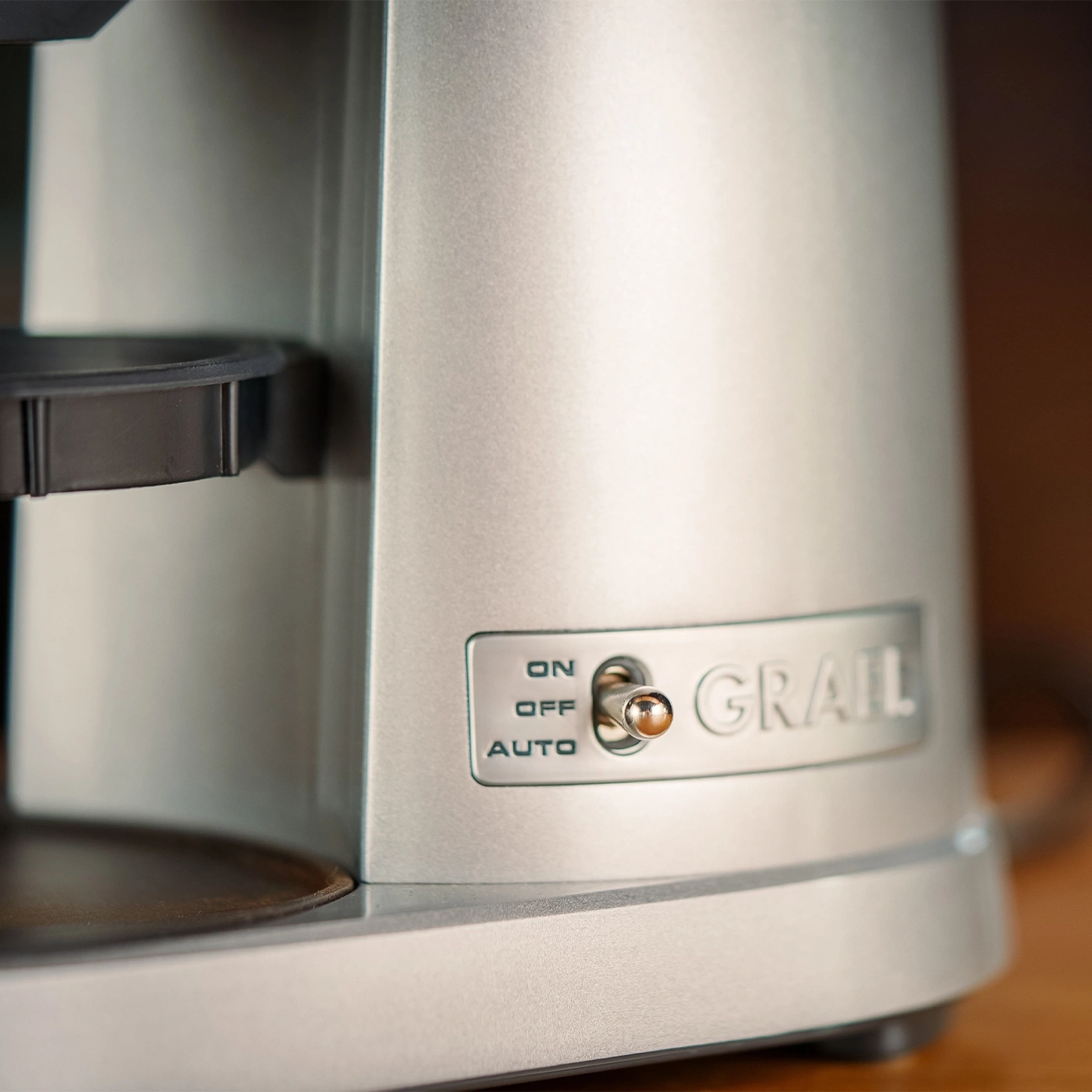 Ein Nahaufnahme-Foto einer silbernen Kaffeemaschine mit einem Schalter und dem Namen GRAIL.