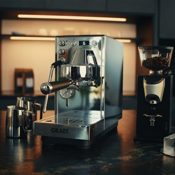 silberene GRAEF Siebträgermaschine, Milchkännchen und schwarze Kaffeemühle daneben