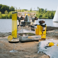 Eine gelbe Espressomaschine und Kaffeemühle am Strand mit einem Getränk.