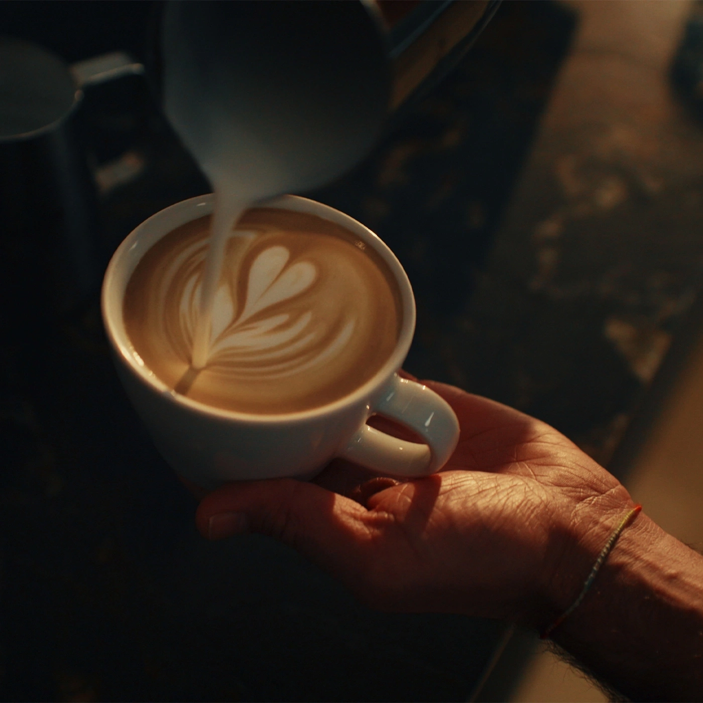 Barista gießt Latte Art in eine Kaffeetasse mit Milchschaum.