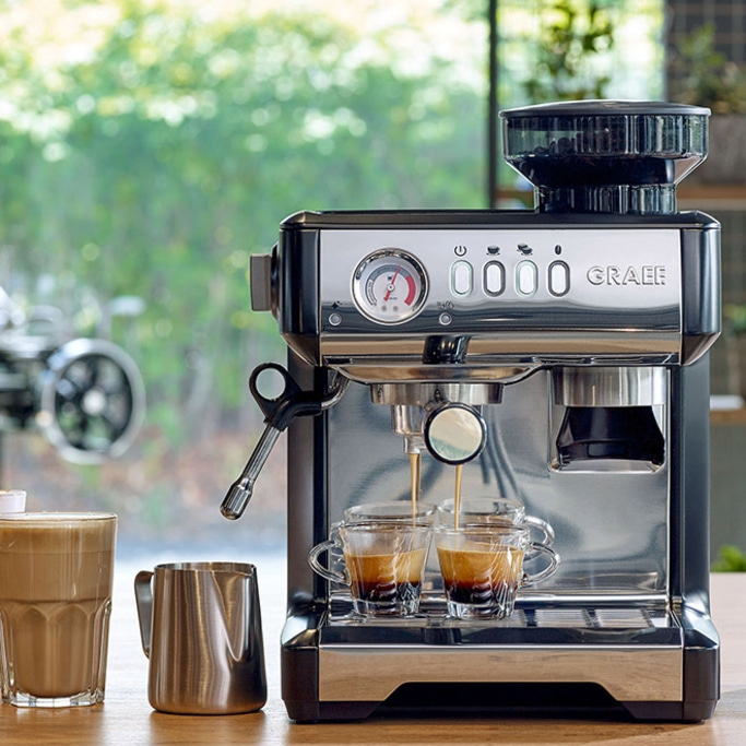 Macchina per espresso che prepara il caffè in due tazze, con lattiera e bicchiere