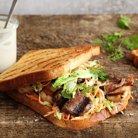Gegrilltes Sandwich mit Fleisch, Gemüse und Sauce auf Holzuntergrund