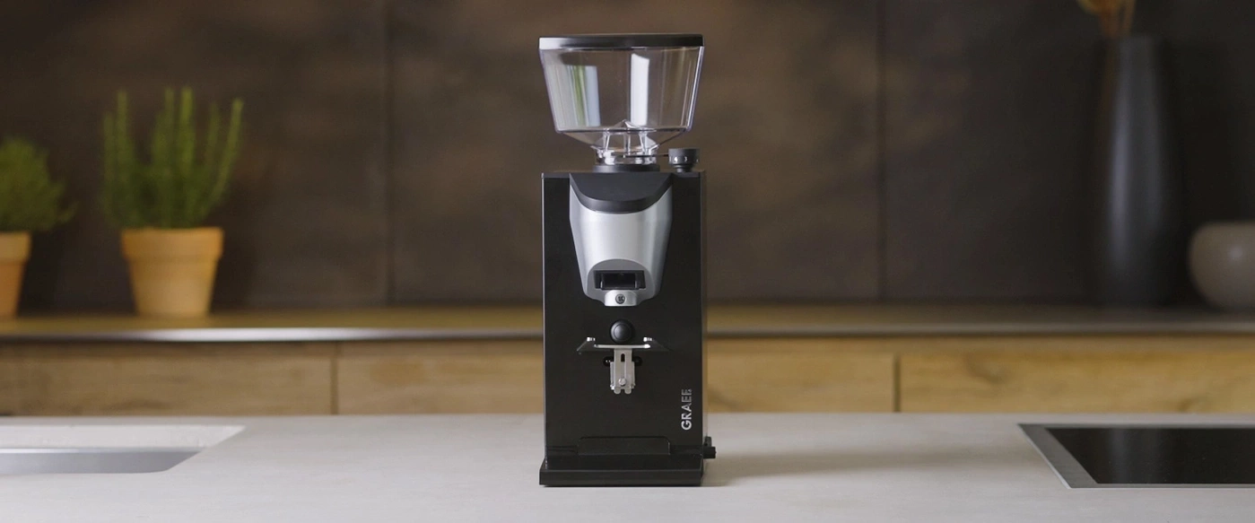 Kaffeemühle auf einer Küchenarbeitsplatte mit Pflanzen und Dekoration im Hintergrund.