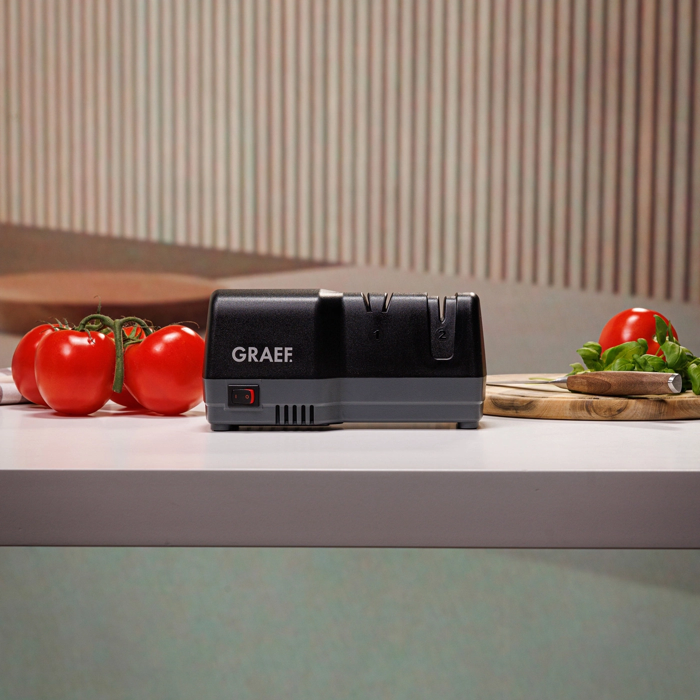 Küchenutensilien: Tomaten, Messer, Schneidebrett und elektrischer Messerschärfer.