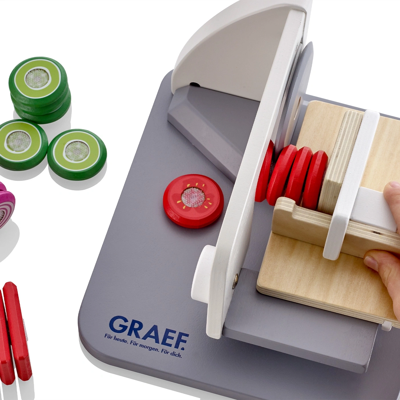 Spielzeug-Gemüseschneider mit Holzgemüse und GRAEF-Logo auf grauem Brett