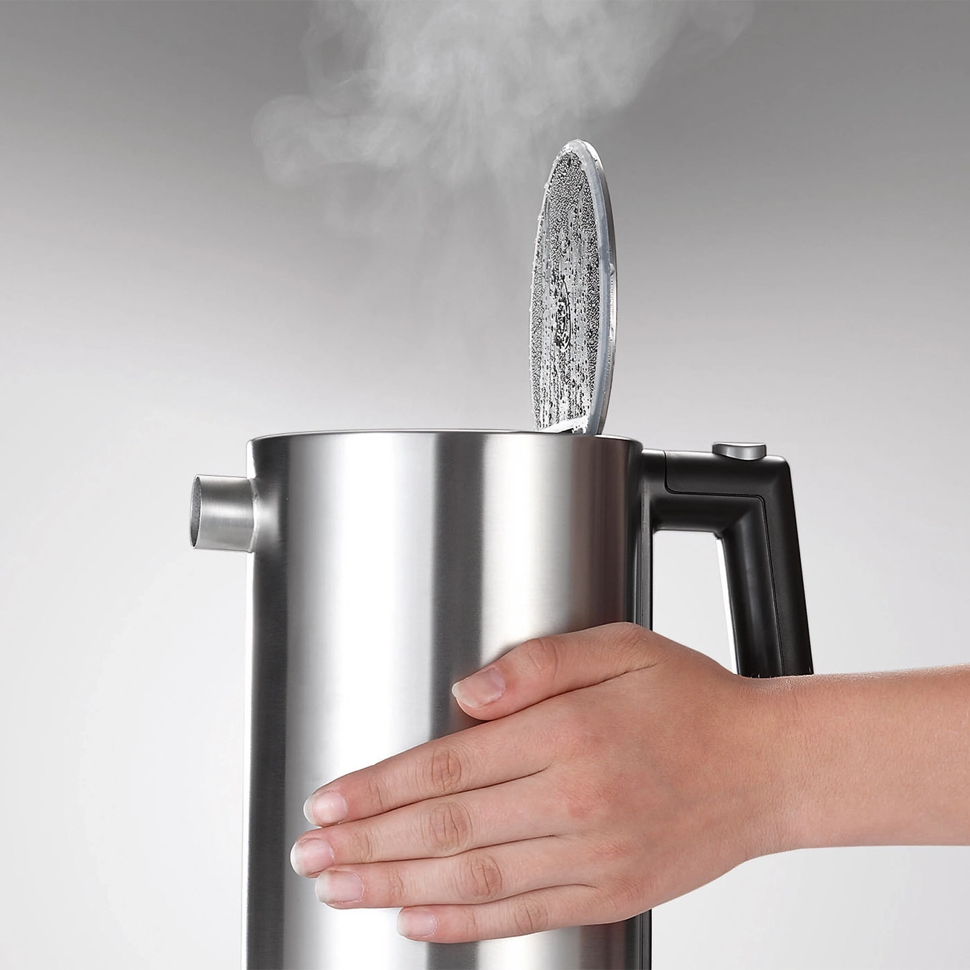 Edelstahl-Wasserkocher mit Dampf, offener Deckel, Hand, grauer Hintergrund, nah