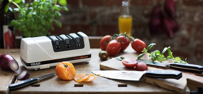 Küchenszene mit Tomaten, Messer, Schleifgerät und Gemüse auf Holzoberfläche