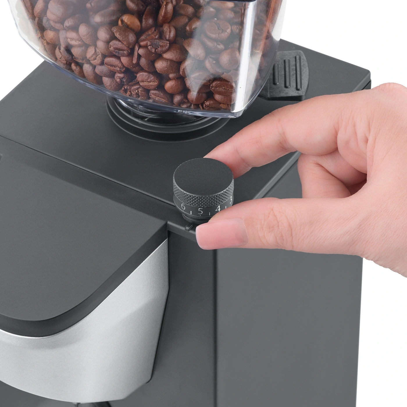 Hand dreht an einem schwarzen Knopf an einer Kaffeemühle mit Kaffeebohnen