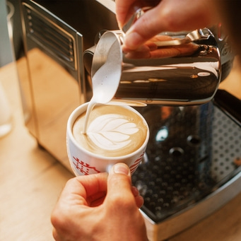Milchschaum in Kaffee gegossen, Latte Art, Siebträgermaschine im Hintergrund