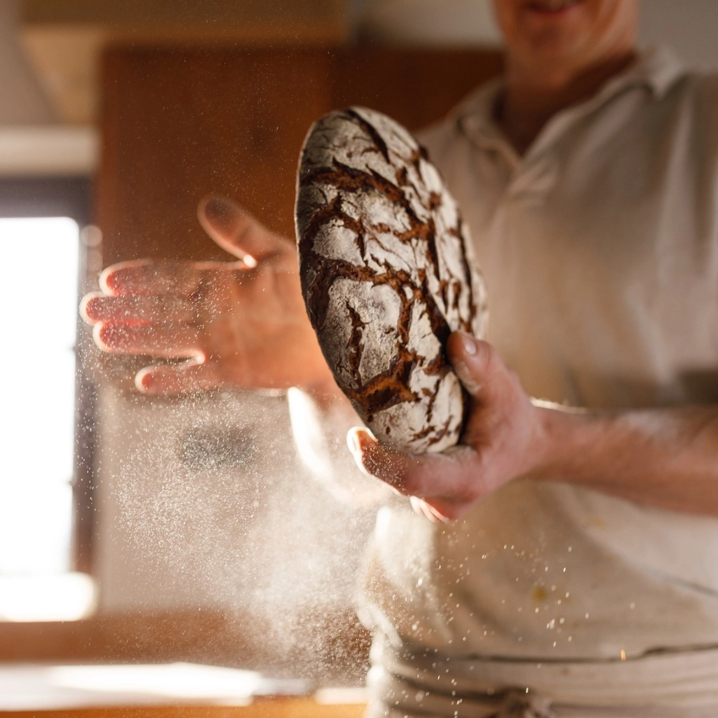 Bäcker hält Brot, Mehlstaub in der Luft, Nahaufnahme, Licht, Küche