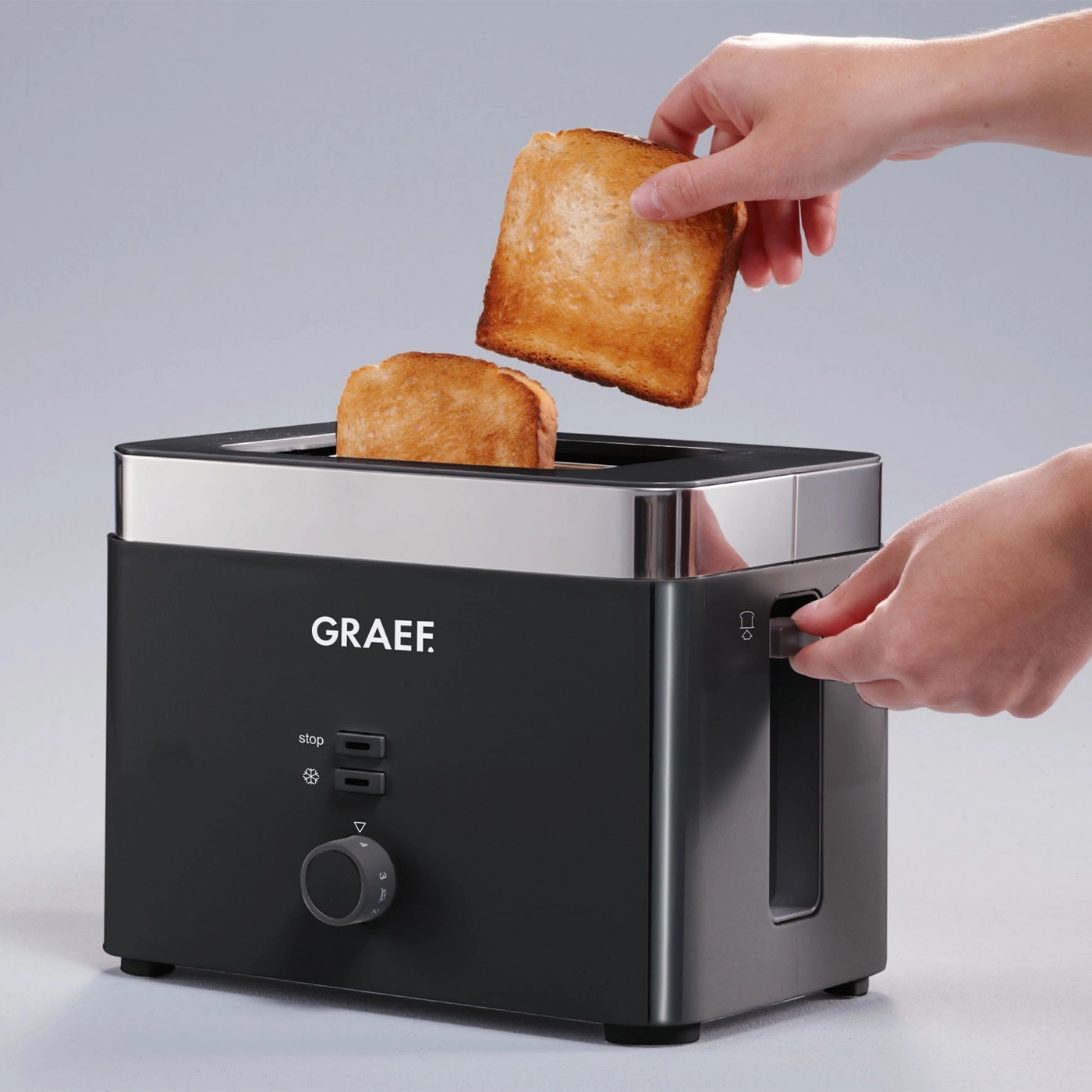 Toaster mit Toastbrot. Person nimmt Toastbrot heraus. Schwarzer Toaster mit silbernen Akzenten.