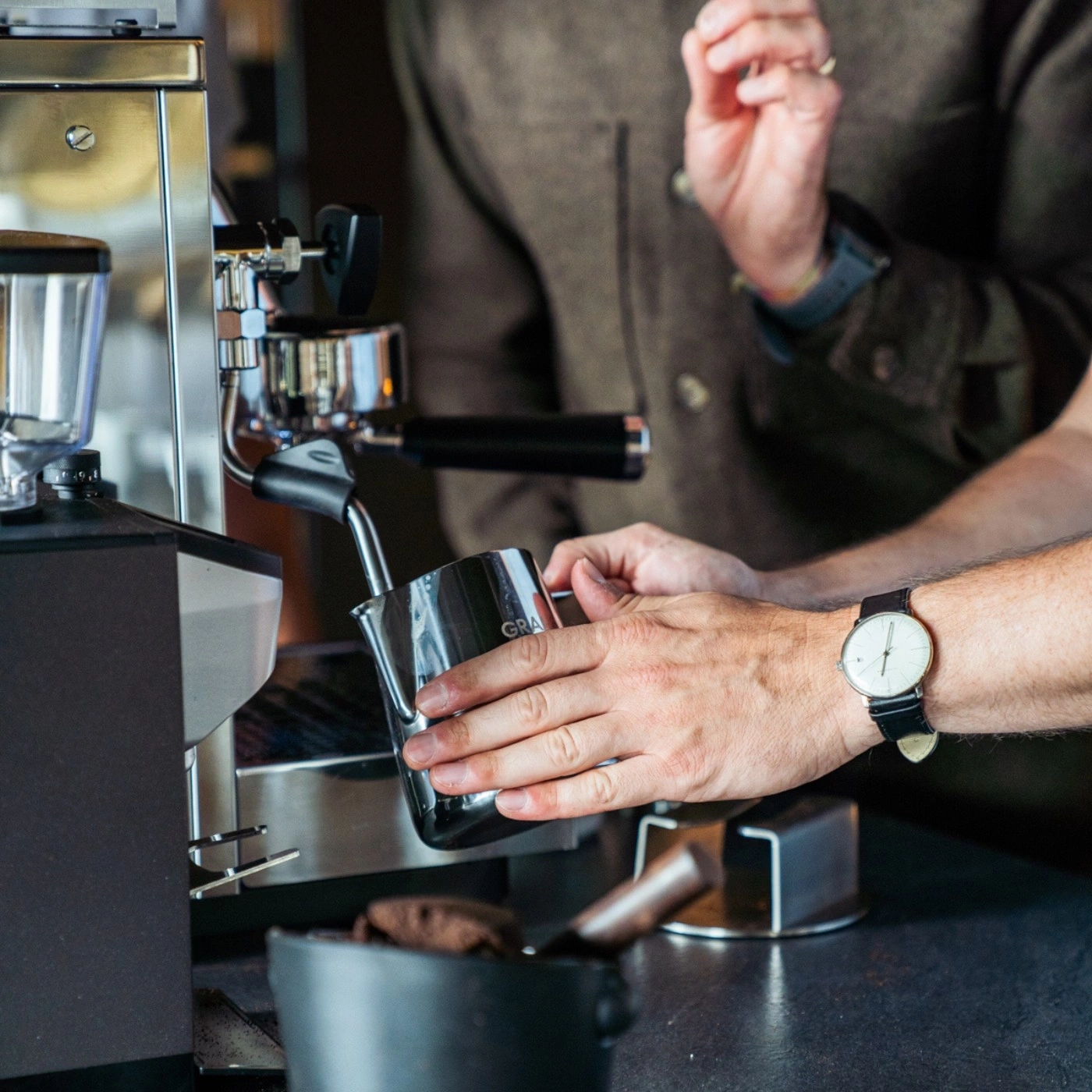 Kaffeezubereitung: Barista gießt Milch in eine Kaffeetasse mit einer Espressomaschine.