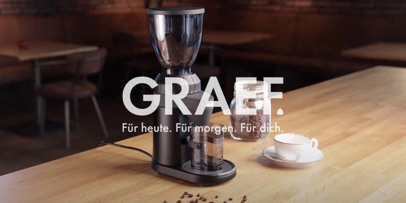 Kaffeemühle mit Kaffeebohnen und Tasse auf einem Holztisch. GRAEF.