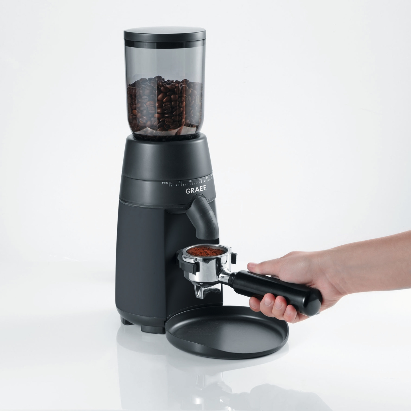 Kaffeemühle mit Kaffeebohnen und gemahlenem Kaffee, Hand hält Siebträger
