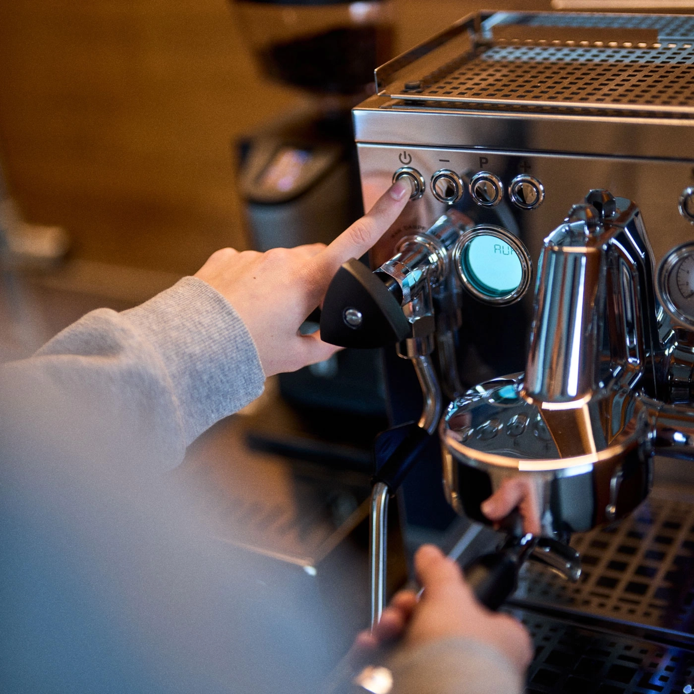 Person drückt Knopf an einer Kaffeemaschine, Nahaufnahme, Hände, Gerät, Edelstahl