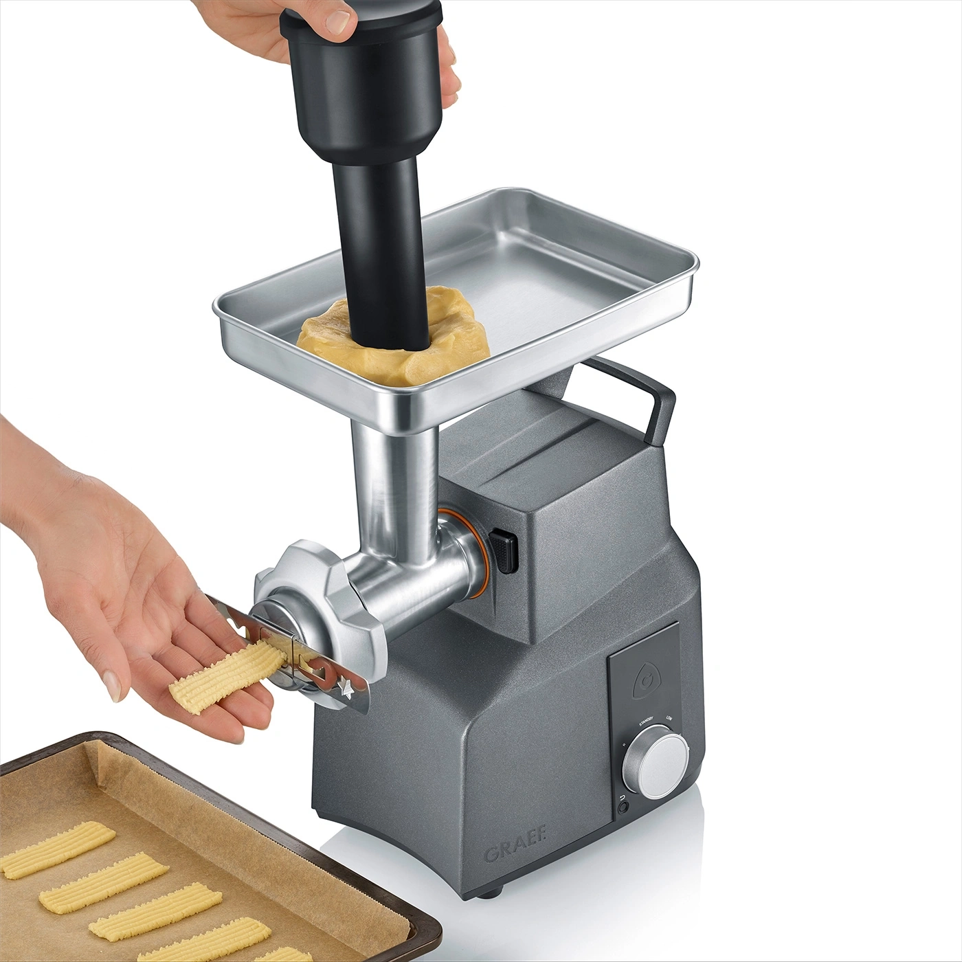 Keksmaschine mit Teig, Händen und Backblech. Graue Maschine, Kekse werden hergestellt.
