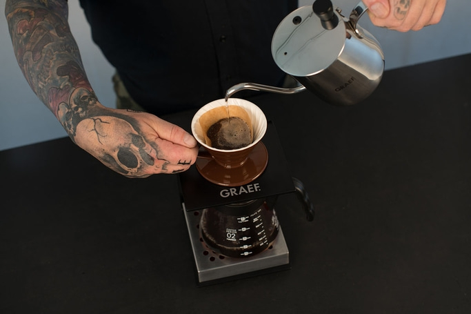 Kaffee wird aufgegossen. Mann mit Tattoo gießt Kaffee ein.
