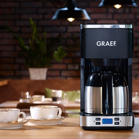 Kaffeemaschine mit Tassen auf einem Holztisch, GRAEF-Logo.