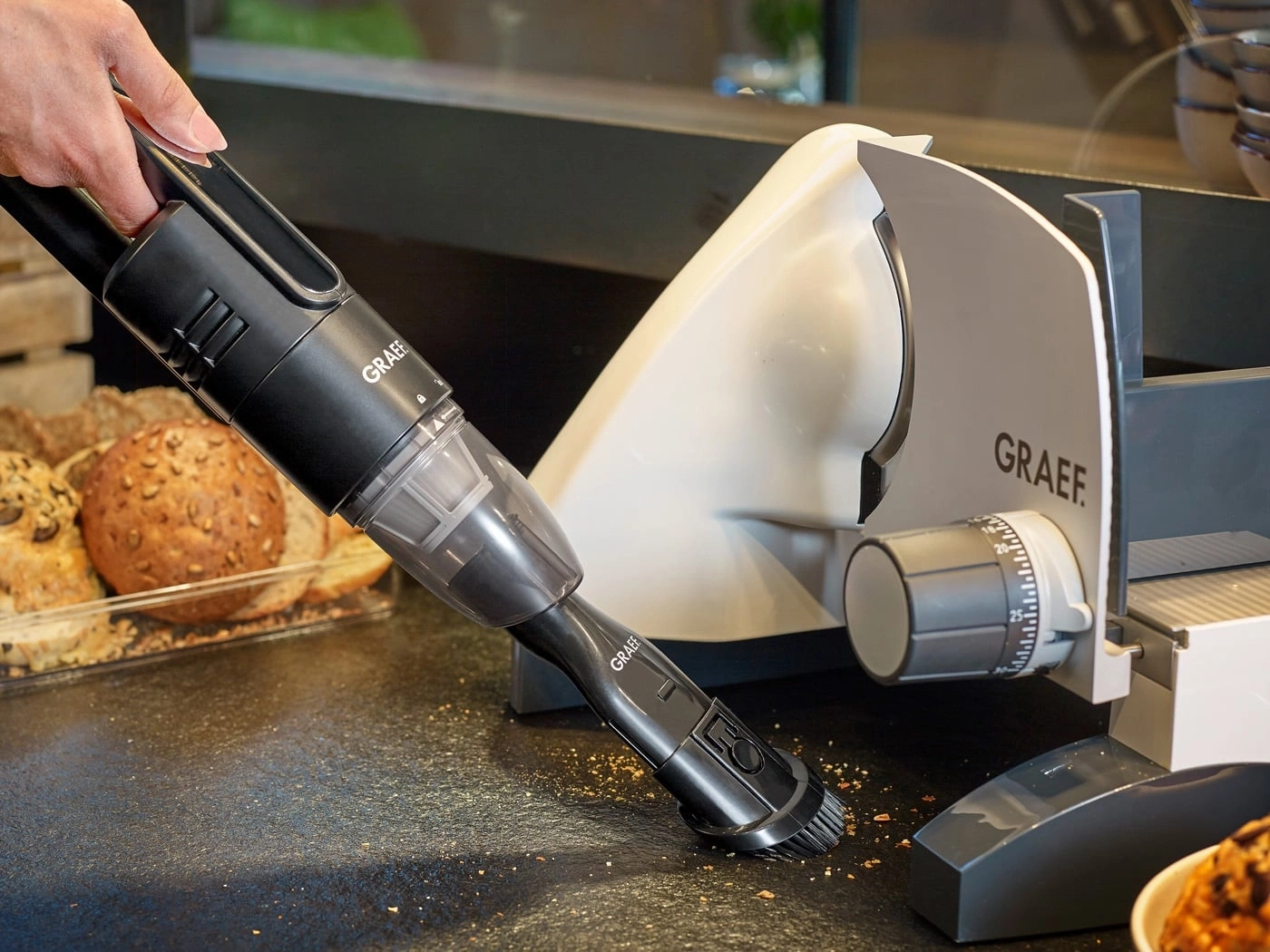 Handstaubsauger reinigt Brotkrümel neben Brotschneidemaschine von Graef.